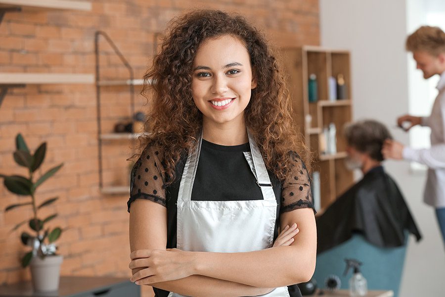 Beauty Salon Insurance - Portrait of a Hairdresser in a Beauty Salon with Client and Fellow Hairdresser Blurred in the Distance